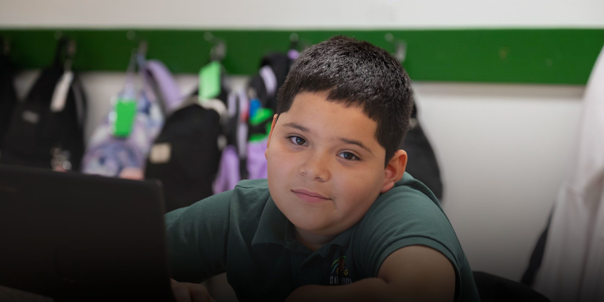 Student in a green school polo seated at a laptop in class.